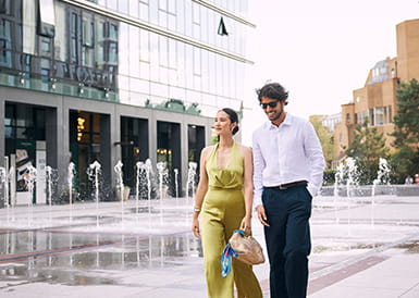 A smartly dressed couple walking near the fountains at London Dock