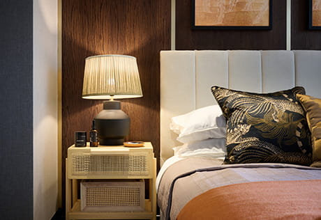 An image of a bedroom with the main focal point being the bedside table with a lamp