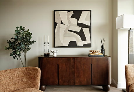 View of armchairs in living space, cabinet drawers against wall with abstract painting above