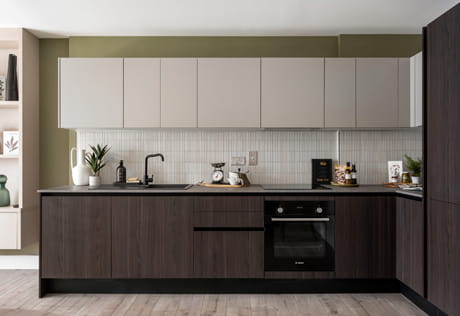 Modern fitted kitchen with dark wood cabinets, pale wall units, black worktop, oven, sink and tiled splashback.