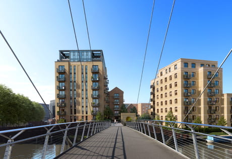 Pedestrian bridge over a canal leading to modern apartment blocks beneath a clear blue sky.
