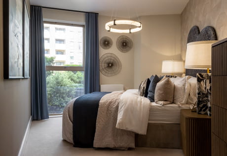 Modern bedroom with double bed, blue curtains, circular wall art and a large window overlooking greenery.
