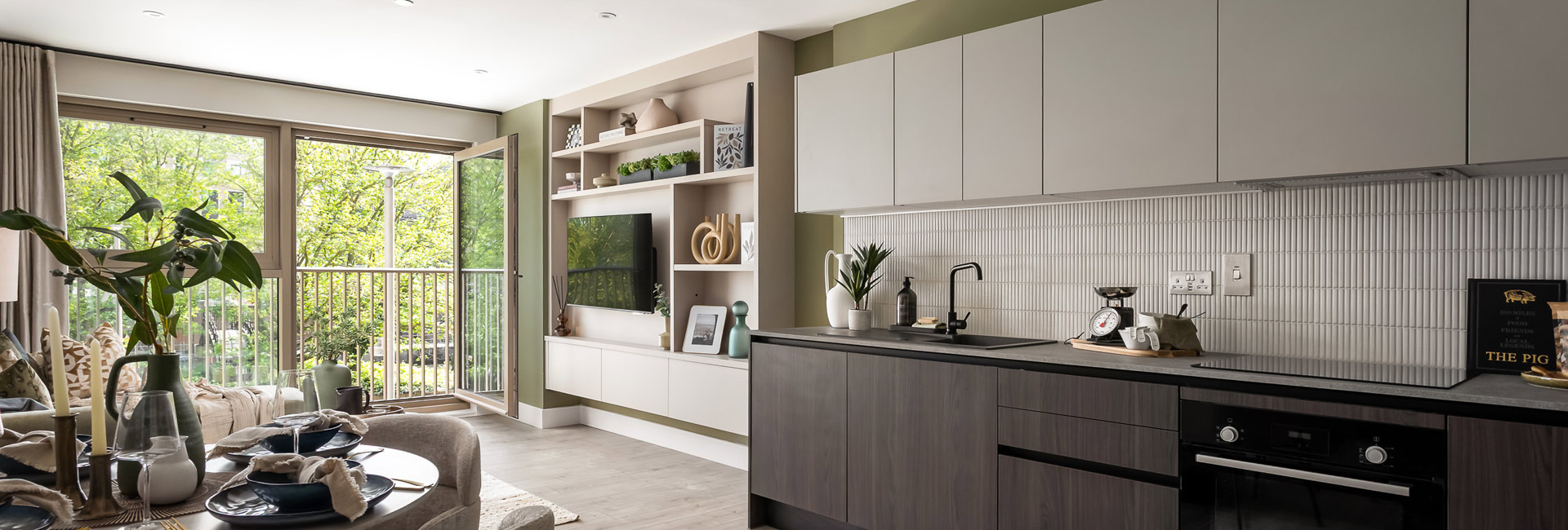 Kitchen with dining table in foreground, decorated in dark tones, living space and balcony doors in background.