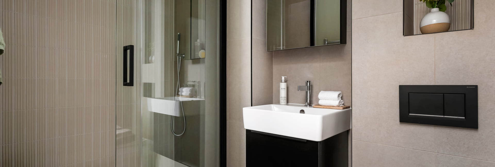 Modern designed bathroom with shower unit, wash basin with wall mirror, beige tiling.