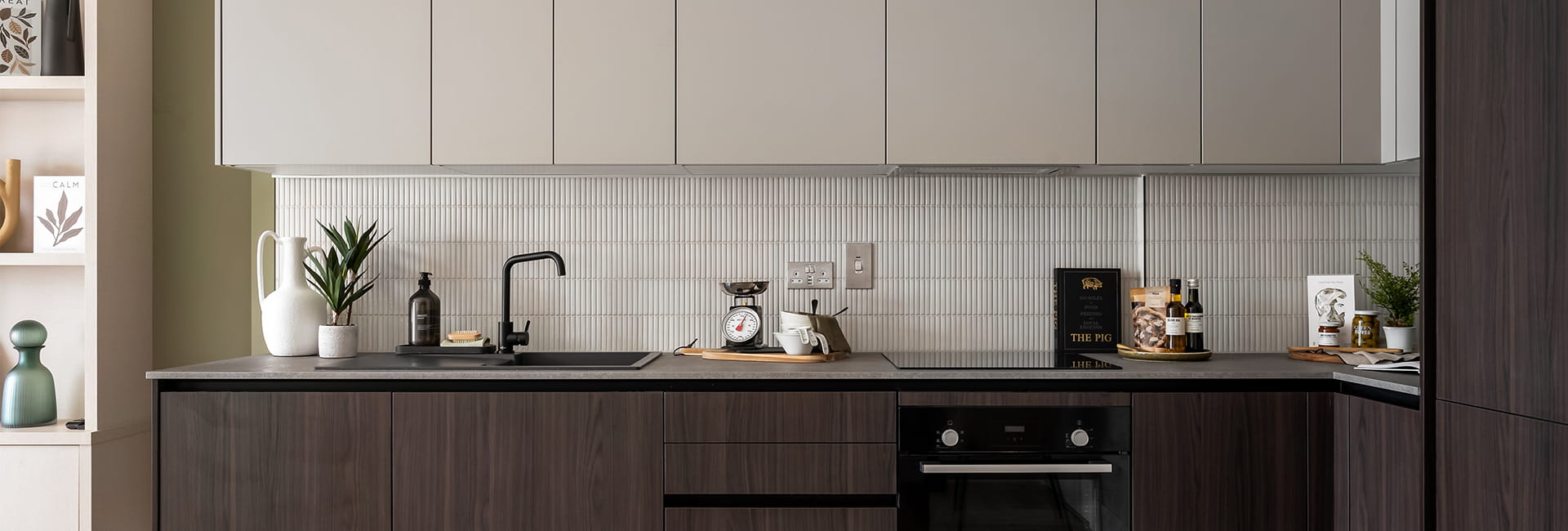 Kitchen area with white splashback tiles and white and mahogany brown cupboards.
