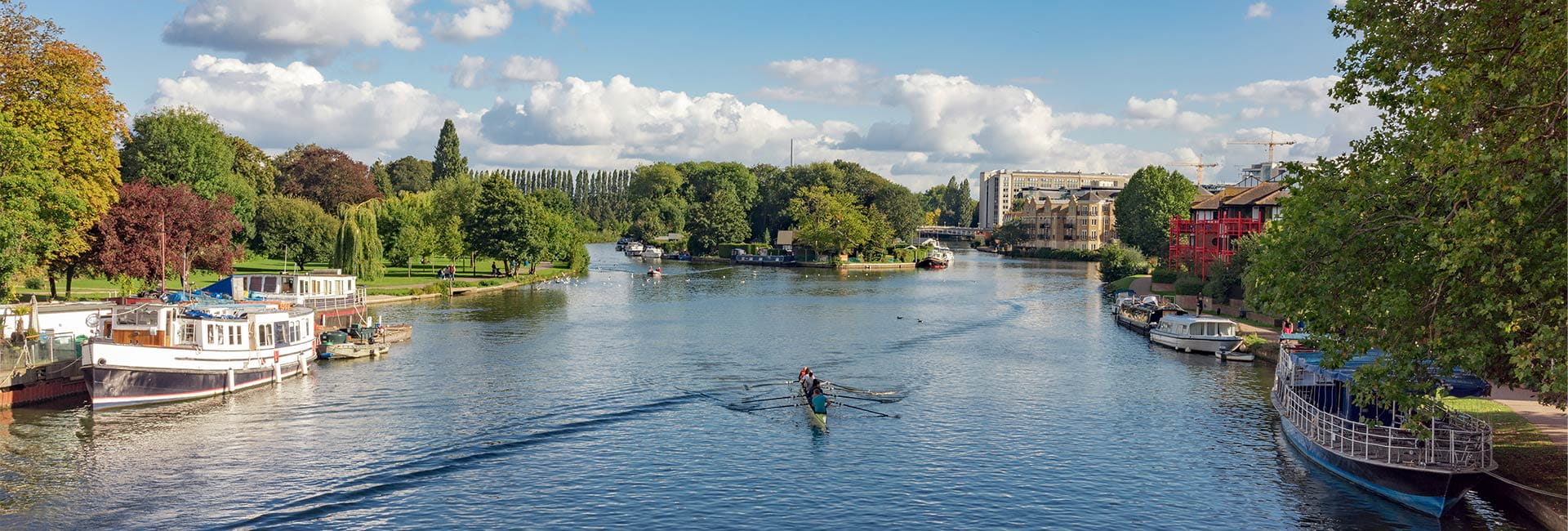 Idyllic, scenic river view with boats on each tree-lined bank, and a kayaker paddling in the middle.