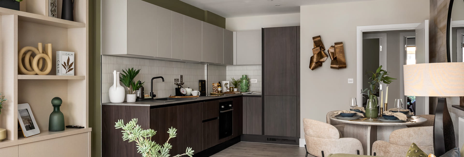 Living space in foreground, kitchen with dining table in background, decorated in neutral tones.