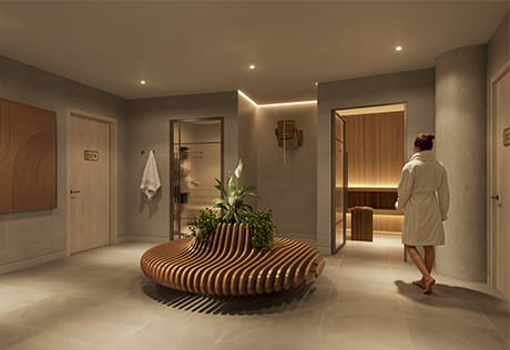 Warmly lit spa lobby with a curved wooden bench, plants, sauna entrance and a woman in a white robe.