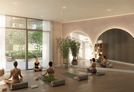 Five women in a bright yoga studio, seated on mats with bolsters, beside tall windows overlooking a garden.