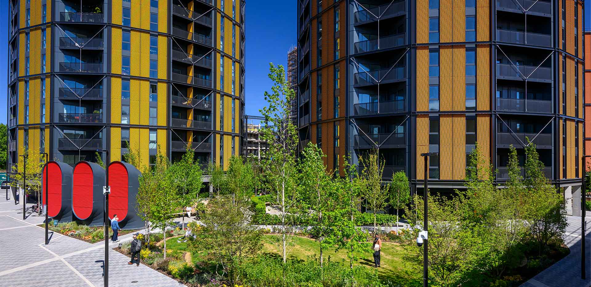 Modern apartment towers overlooking a landscaped courtyard with trees, paths and a red sculptural installation.