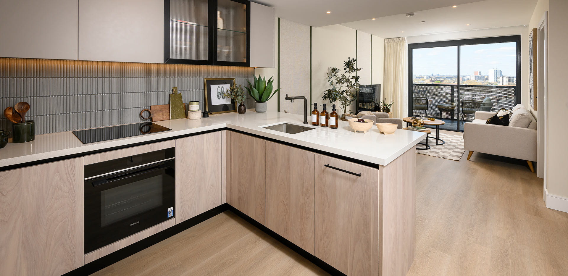 Kitchen with island, light brown beige tones, living space and balcony doors in background.