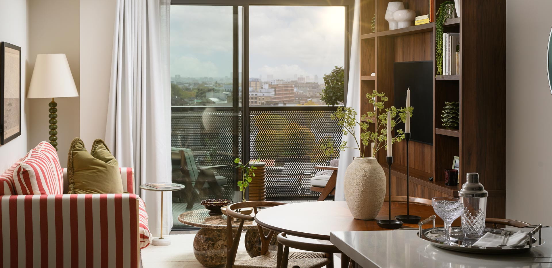 Stylish modern living room with striped sofa, dining table, wooden shelving and balcony city view.