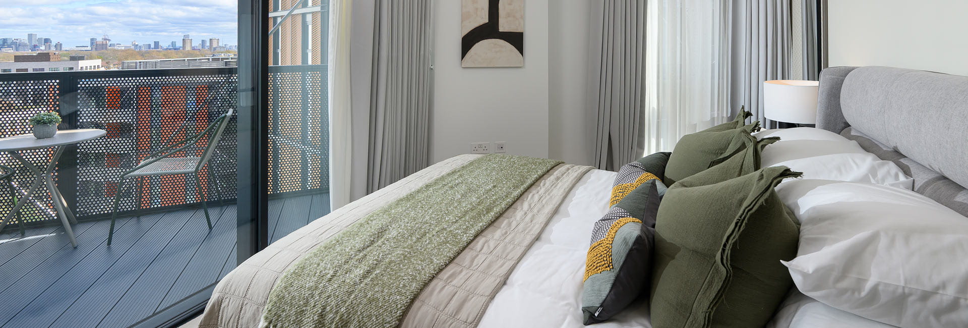 Bedroom designed in greens and greys and white, facing balcony sliding doors overlooking city view