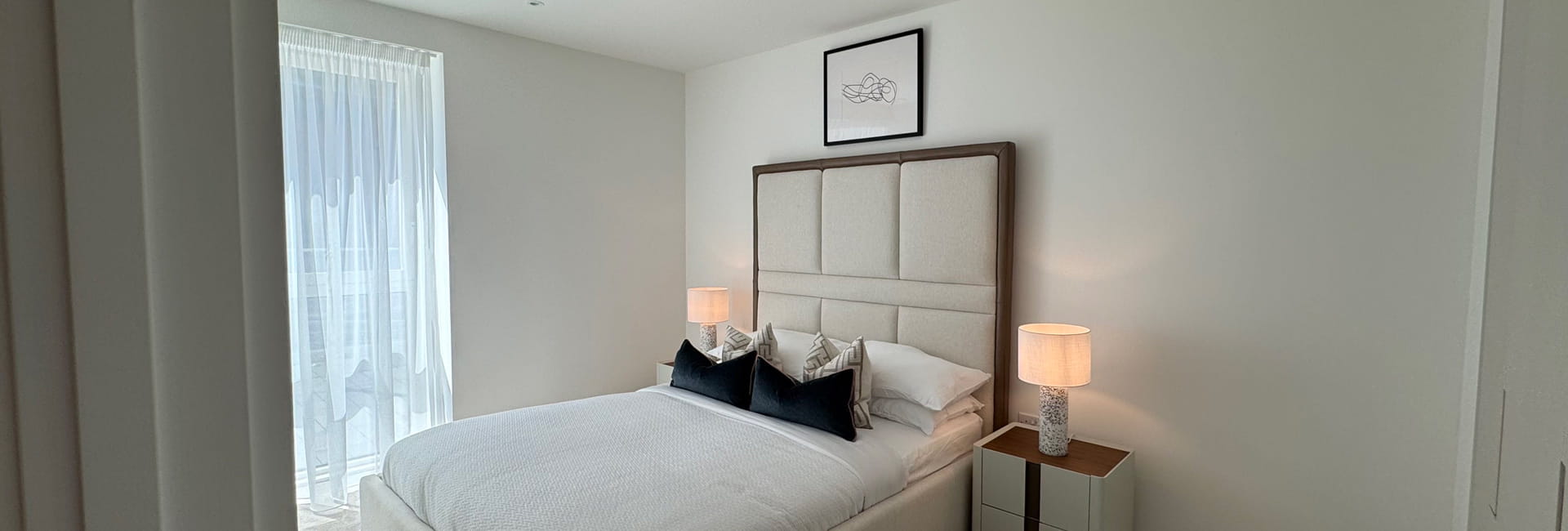 Double bed with contemporary design, off-white walls, bedside tables and wall hanging.