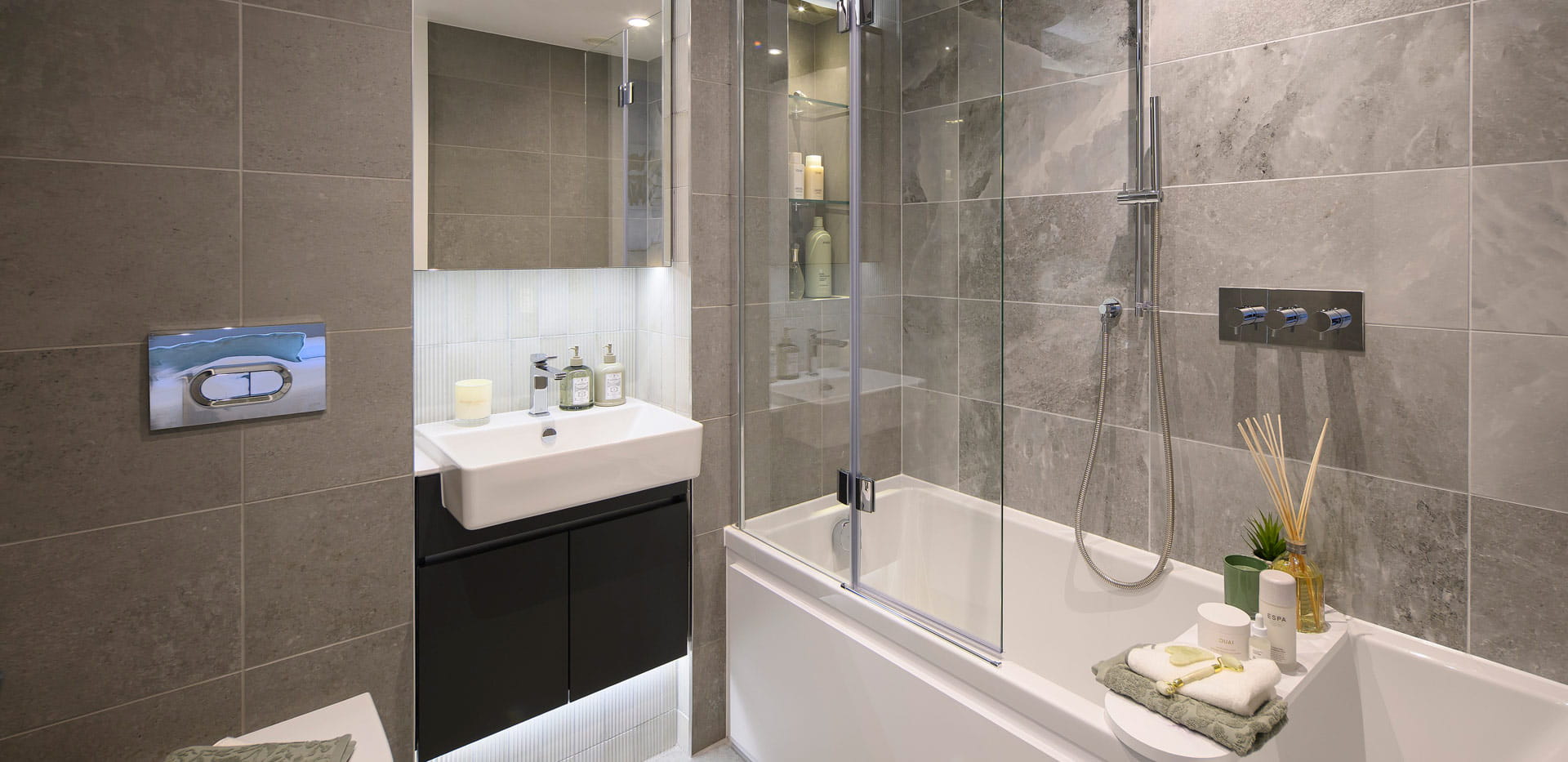 Modern designed bathroom with shower over bath, wash basin with wall mirror, toilet and cabinet space