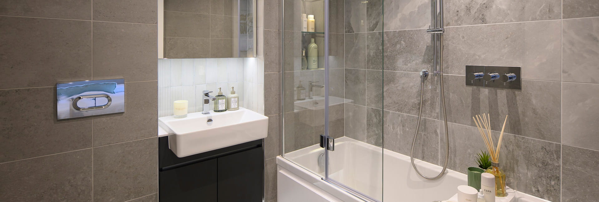Modern designed bathroom with shower over bath, wash basin with wall mirror, toilet and cabinet space