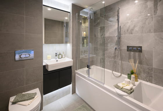 Modern designed bathroom with shower over bath, wash basin with wall mirror, toilet and cabinet space