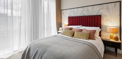 Bedroom with central double bed with red headboard and neutral coloured bedding