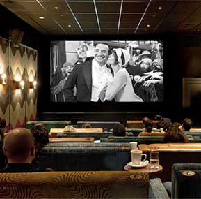 People watching a black and white movie in cinema setting with sofa seating