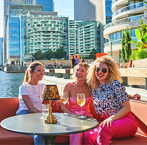 Ladies enjoying drinks in an outdoor setting tall buildings and river in background