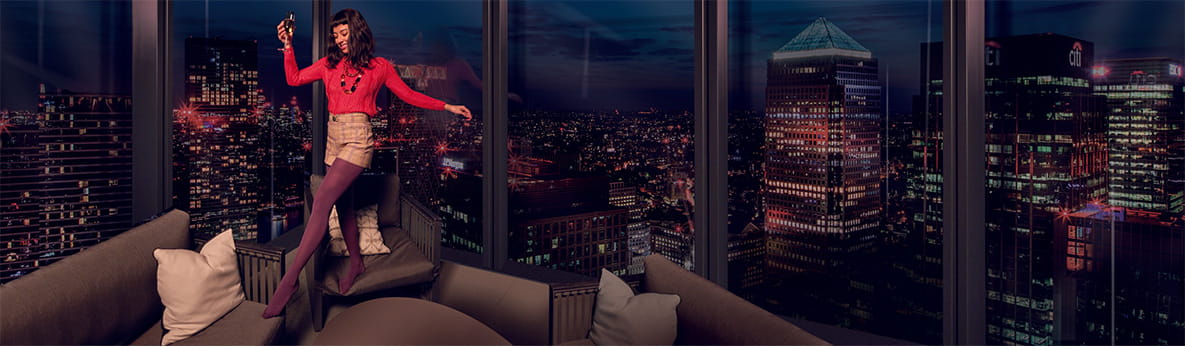 An image of a woman standing on a sofa enjoying a drink