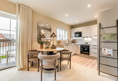 A wideshot of circular dining table, kitchenette in background, balcony doors and newspaper rack