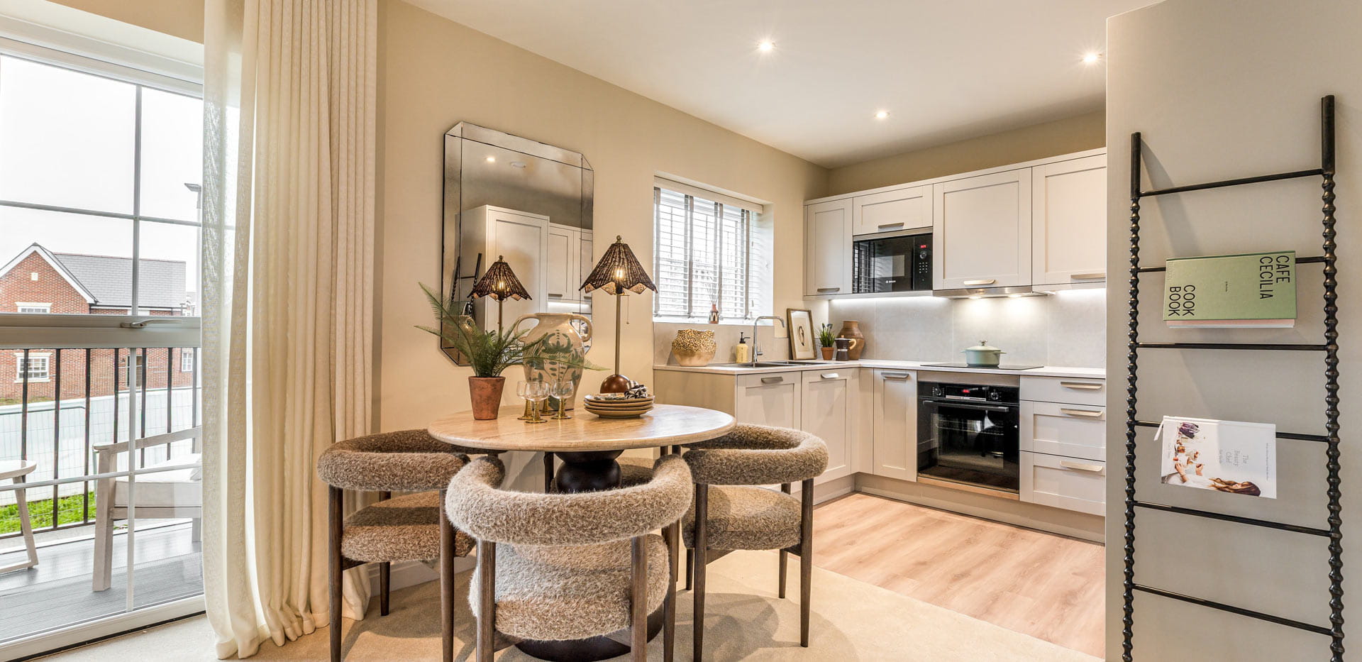 A wideshot of circular dining table, kitchenette in background, balcony doors and newspaper rack