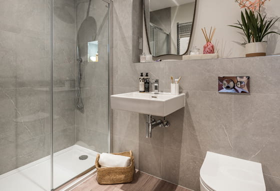 Shower unit in grey tiles, wash basin with wall mirror.