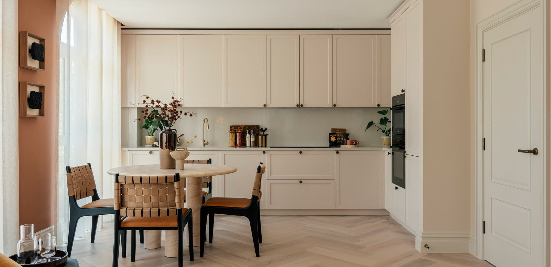 Dining table in foreground, kitchen with white panels.