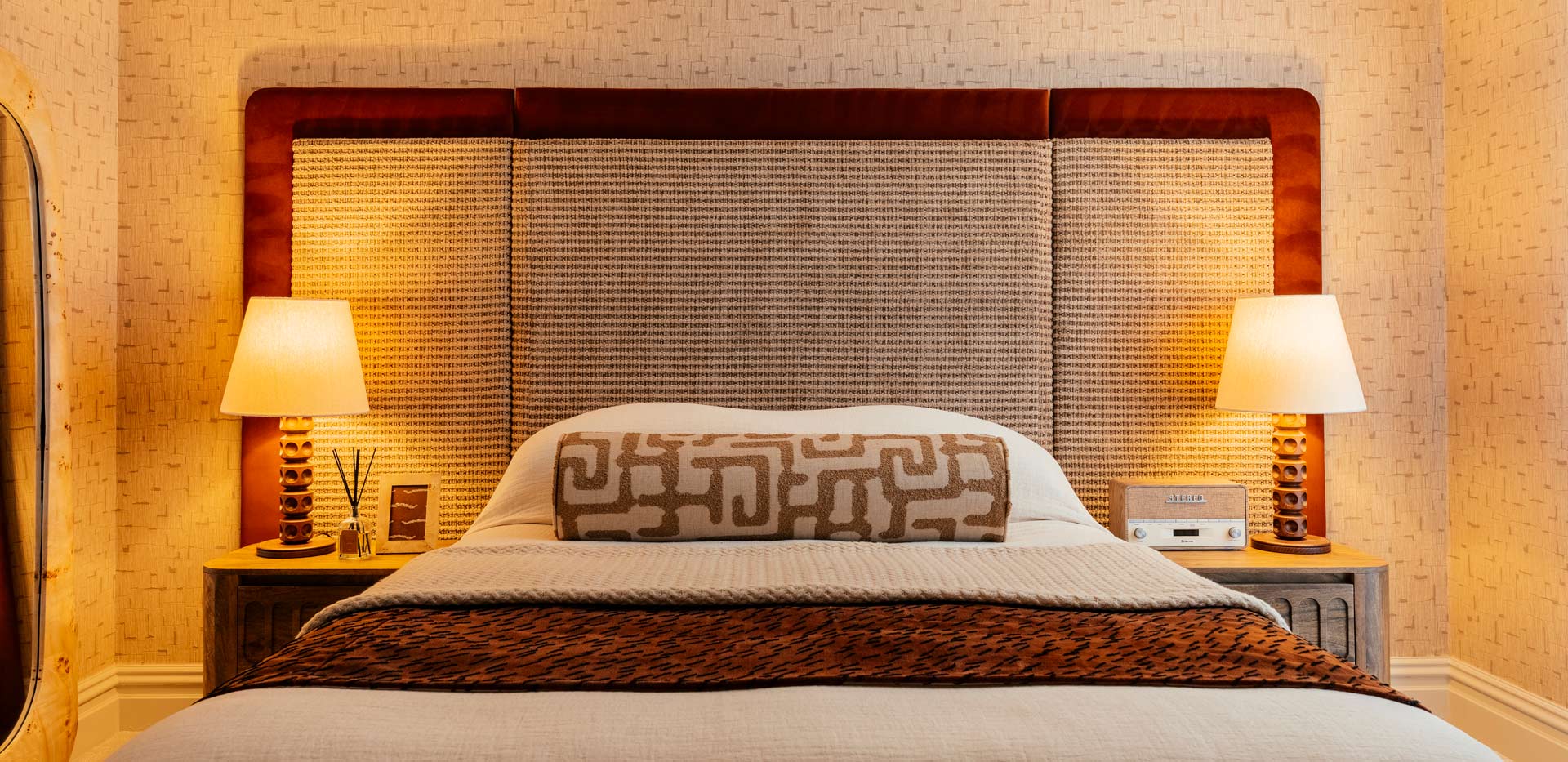 Double bed with tall and wide headboard, wall mirror, ottoman and bedside tables.