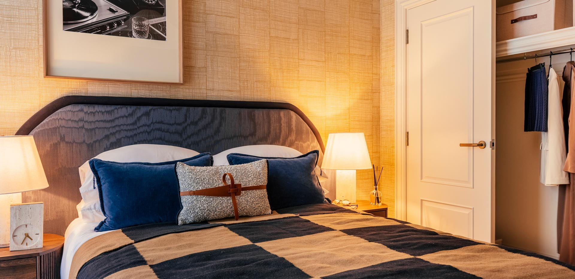Chequered pattern quilt on bed, wall hanging above, bedside tables and built-in wardrobe with sliding door.