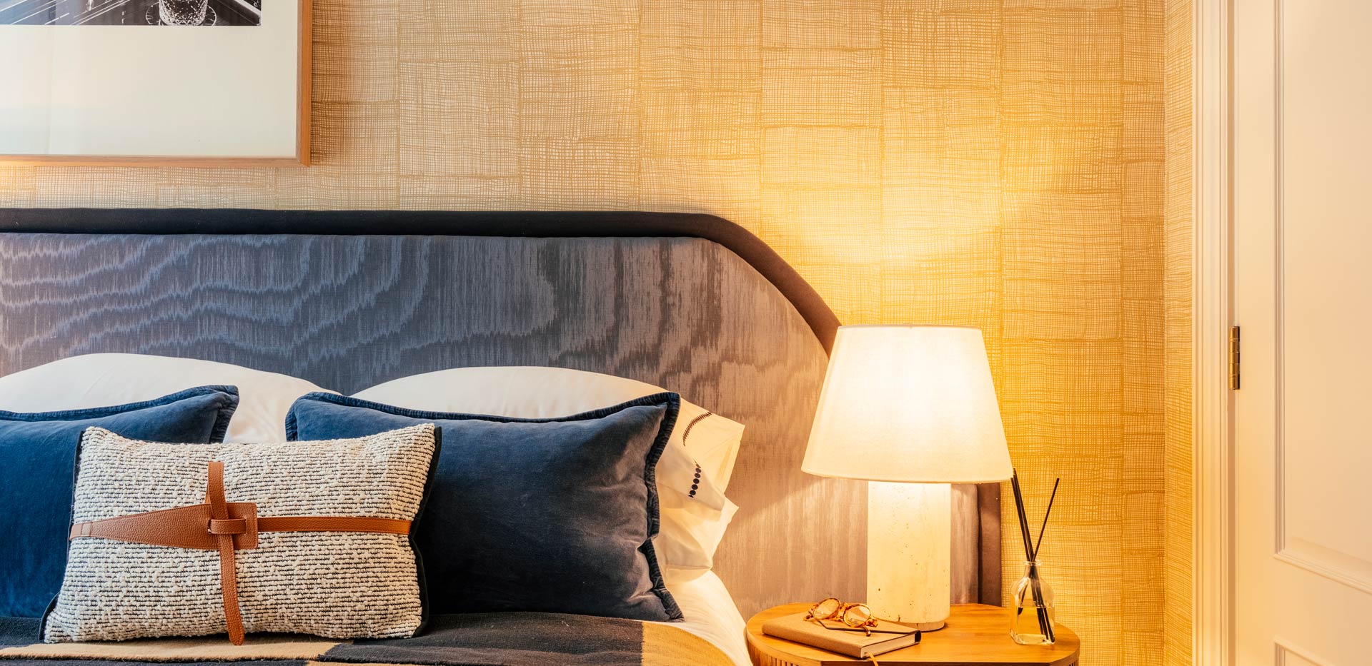 Chequered pattern quilt on bed, wall hanging above, bedside table with lamp.
