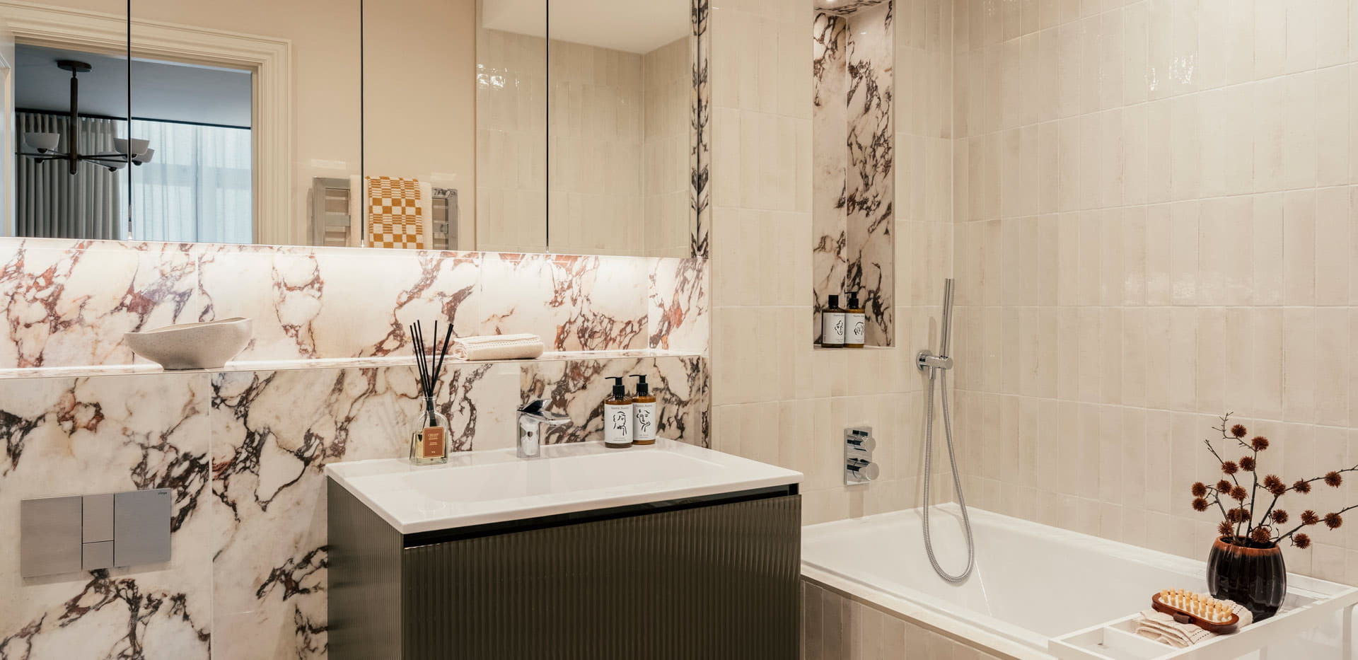 Bathroom with shower over bath, floral pattern on some tiling, wash basin with cabinet mirror and shelving above.