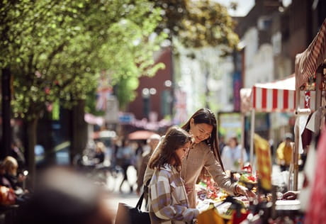 Adult and child at an open street market on a sunny day.