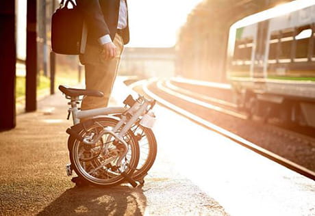 An image of a person standing at the station with a bike folded up