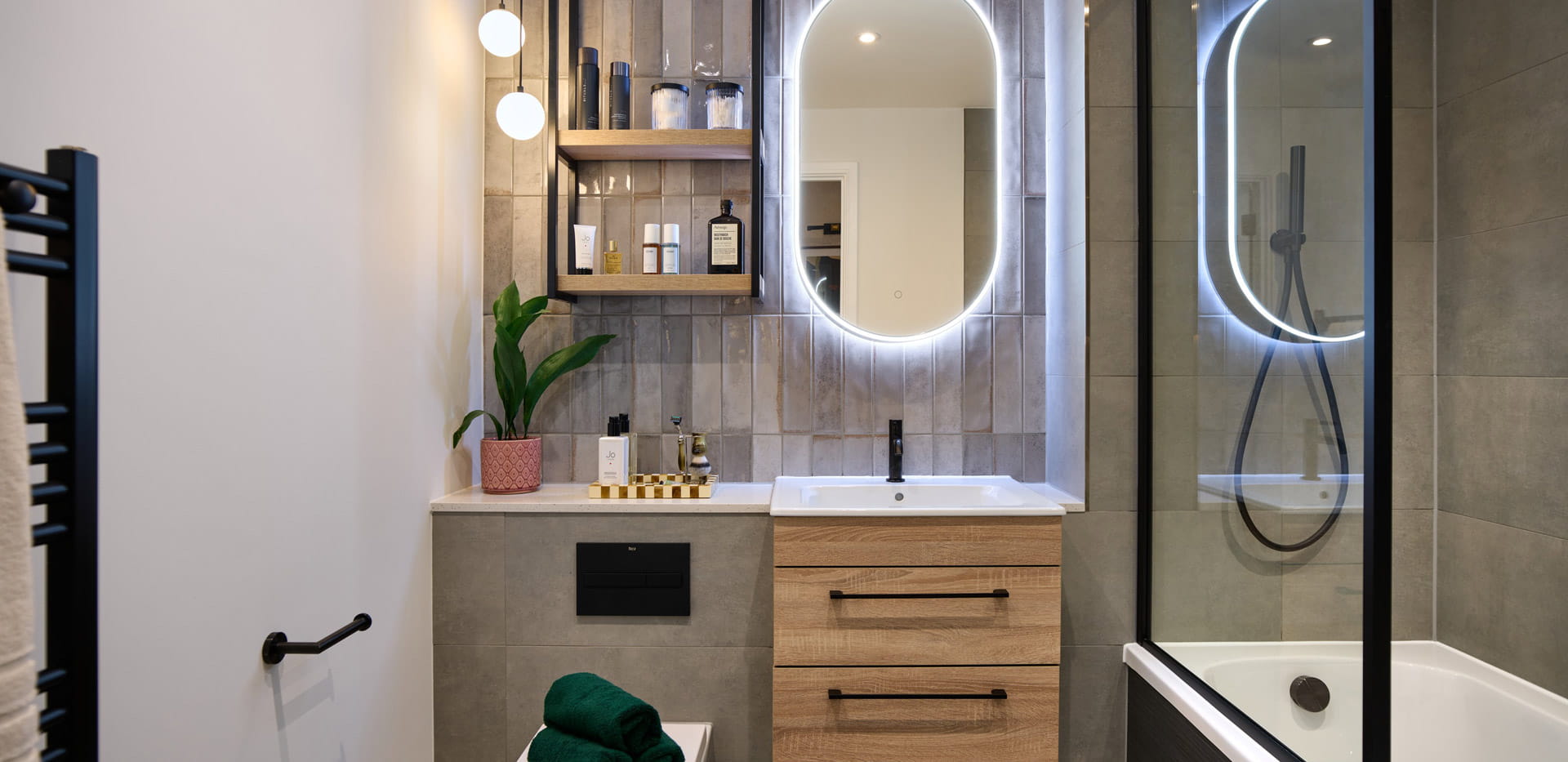 Modern designed shower over bath with black trim, vanity lighting around mirror, shelving space for toiletries 