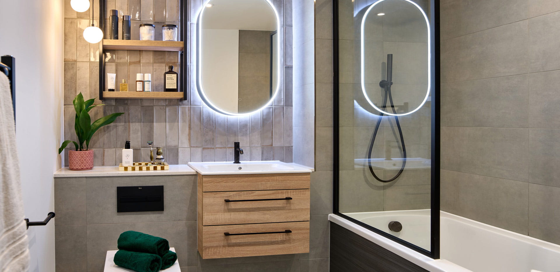 Modern designed shower over bath with black trim, vanity lighting around mirror, shelving space for toiletries 