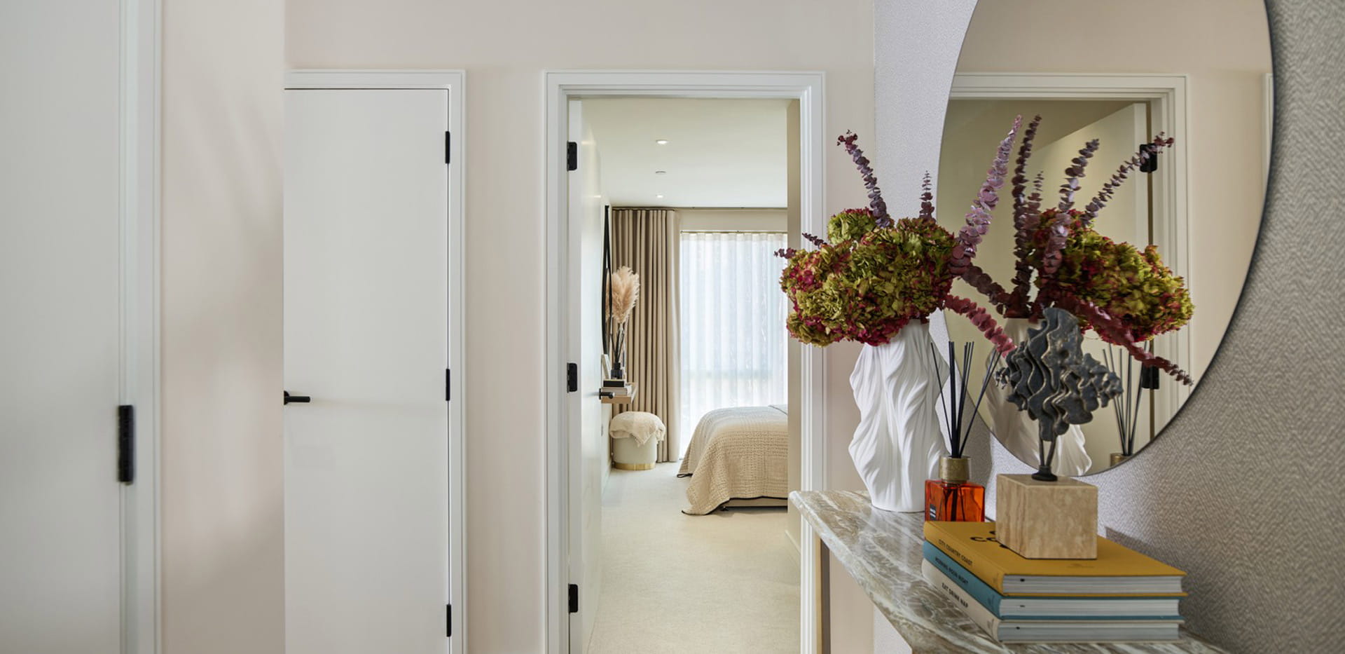 Hallway with console table, decorated with stacked books and flowers, wall hanging mirror.