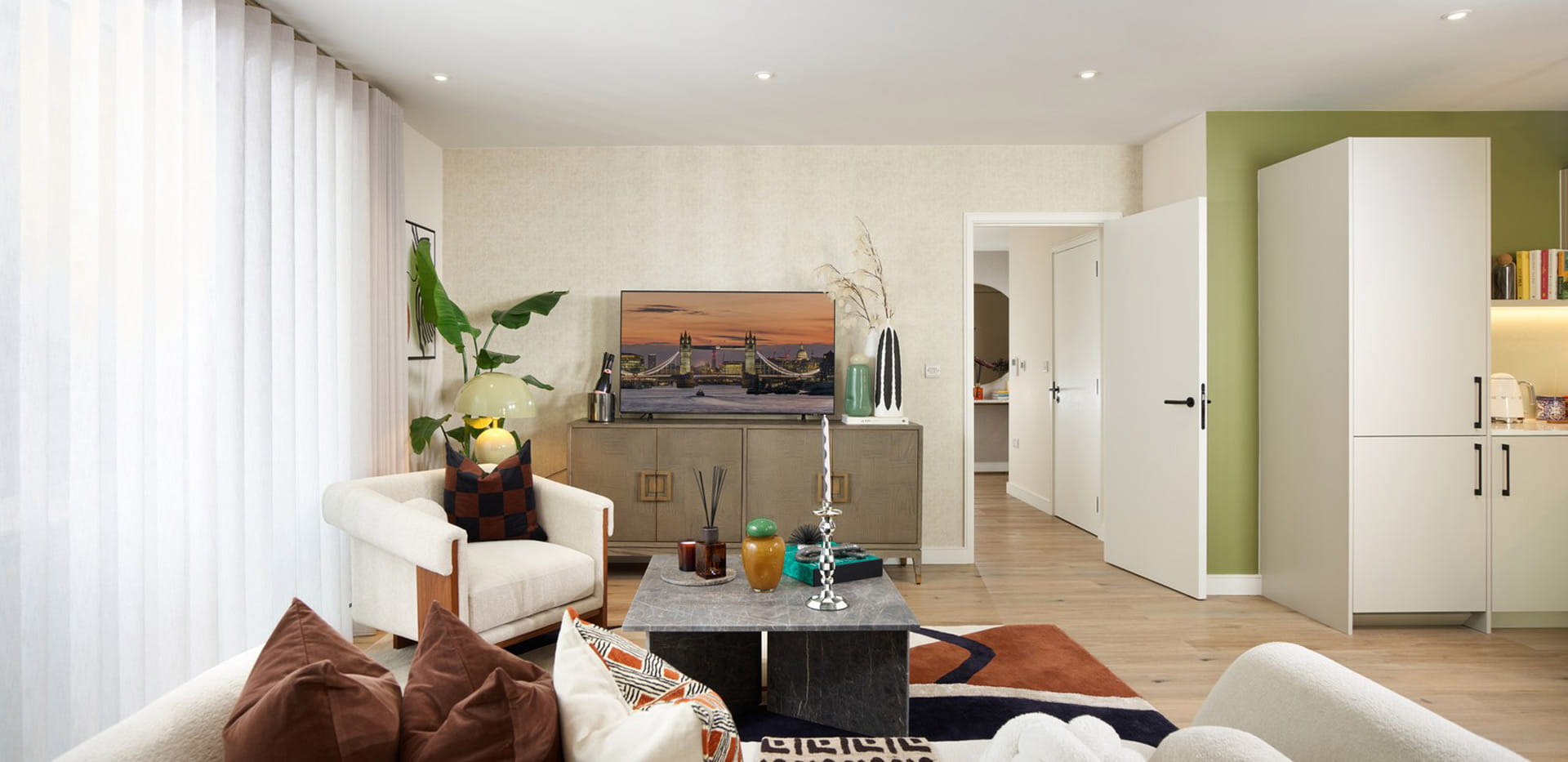 Modern designed living space with sofa and coffee table, TV unit, adjacent to kitchen.