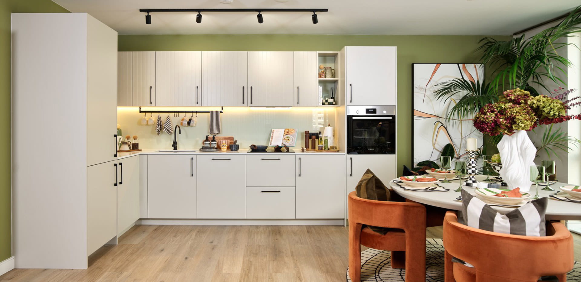 Decorated dining table in foreground, kitchenette with white panels and modern comfort appliances, in background.