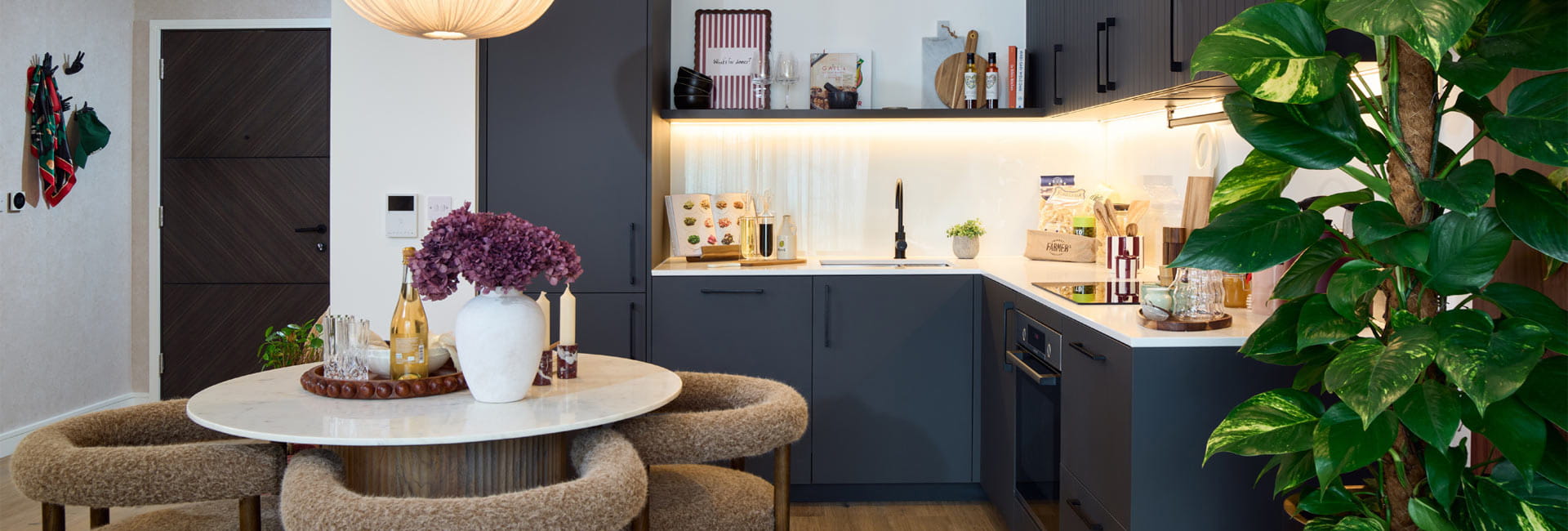 Kitchen, navy blue cupboard panels and white countertops, modern appliances, dining table in foreground.