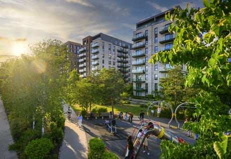 CGI of a well maintained childrens playground set amongst greenery and new build flats in the background.