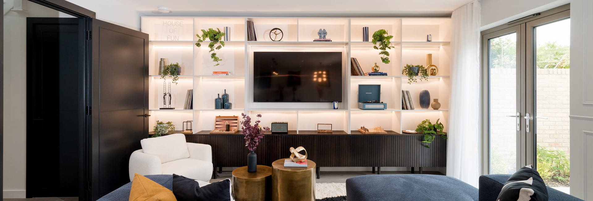 Living space with wall mounted TV surrounded by shelving units, chaise lounge and patio doors