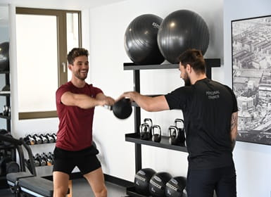 Male and male trainer exercising in an indoor gym weights area.