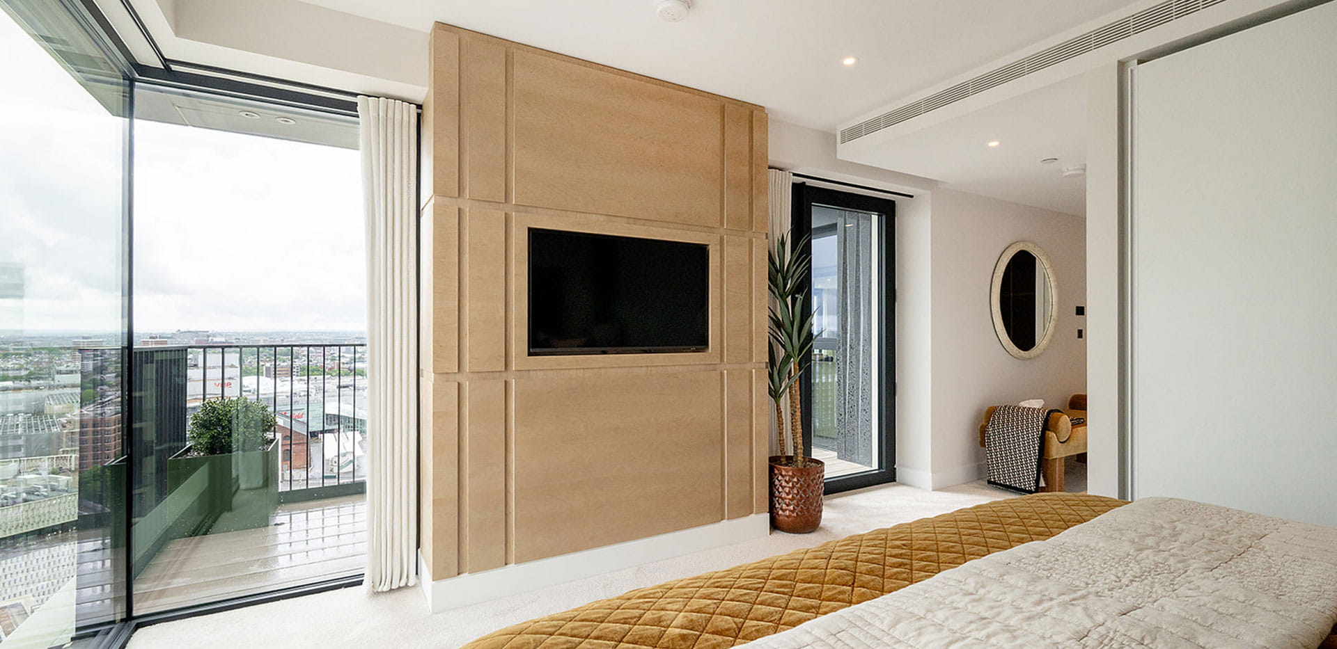Bedroom with TV mounted into pillar wall, wraparound tall windows overlooking balcony.