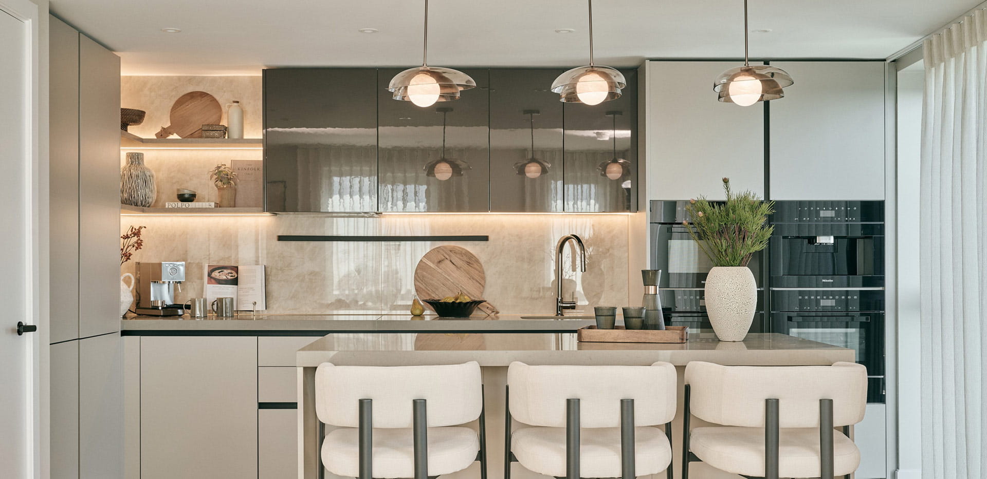 Modern designed kitchen, suspended low-hanging lights, light grey cupboards and panels.