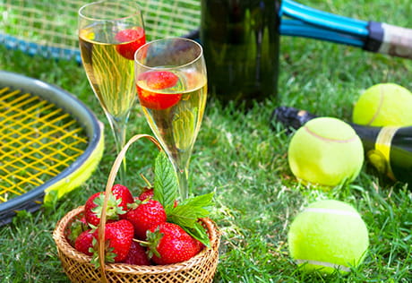 An image of tennis equipment and glasses of alcohol on grass