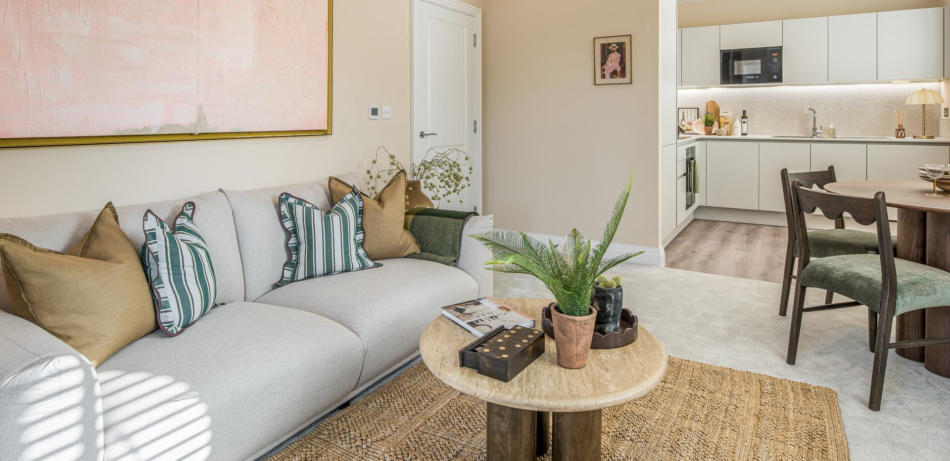 Living room and dining space decorated in beige and light greens and browns with kitchenette in background