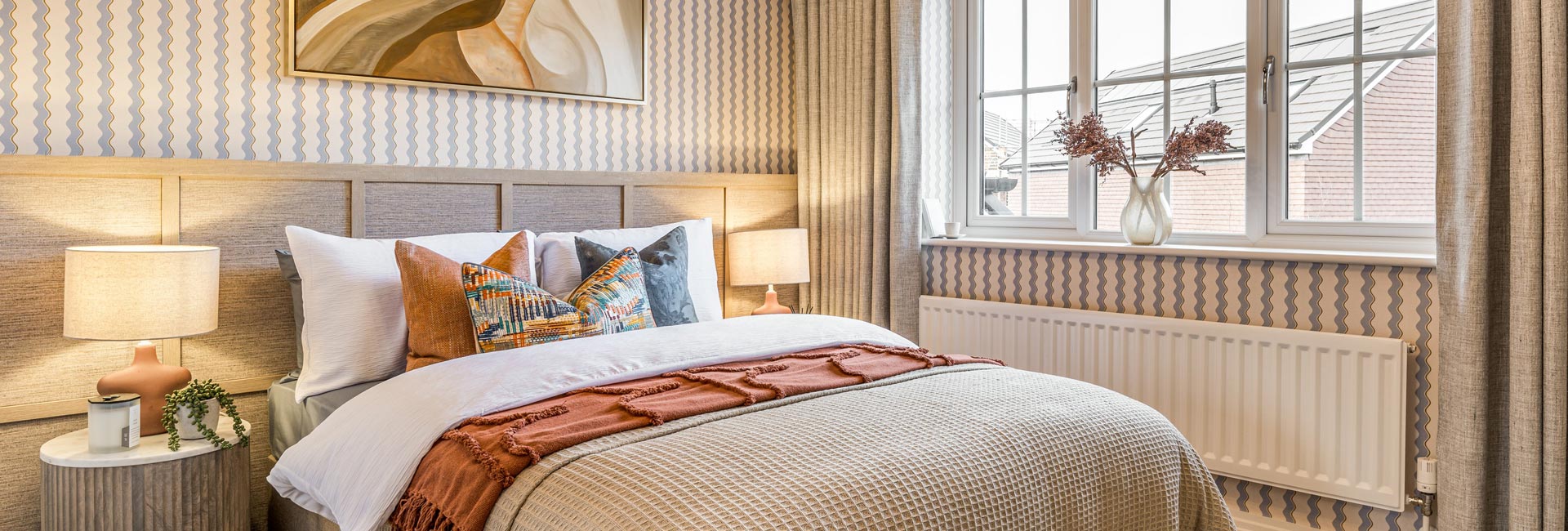View of a doubled decorated with wide wooden headboard, with bedside tables and wall hanging