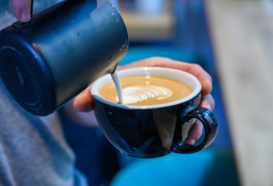 Barista pouring heated, frothy milk into a coffee cup